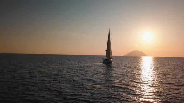 Aerial View on White Sailboat Floating in Mediterranean Sea Against Lipari Island. Sun Reflecting in