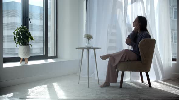 Young Woman with Long Hair Sits in a Chair and Puts on Wireless Headphones