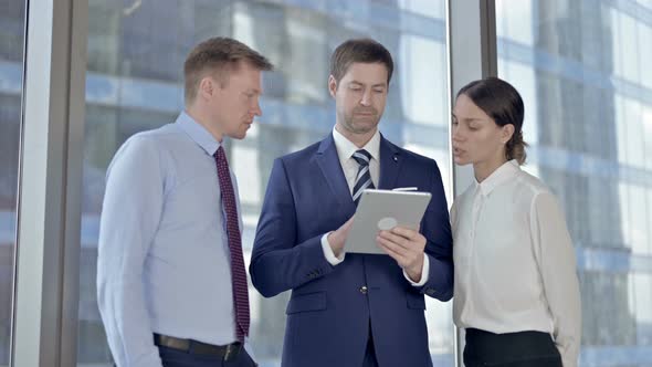 Middle Aged Businessman Scrolling on Tablet with His Assistants in Office