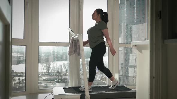Confident young woman is walking on running machine at home in balcony