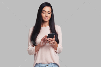 g her smart phone while standing against grey background