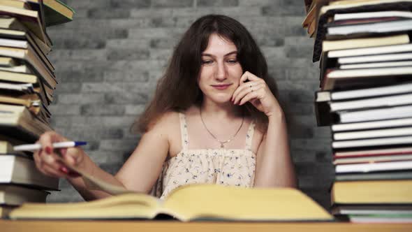 Tired Female Student Reading Among Books. Pensive Young Woman Sitting at Table with Pile of Book and