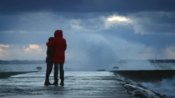 Girl and Boy Hug and Looking at Storm Waves Crashing to the Pier