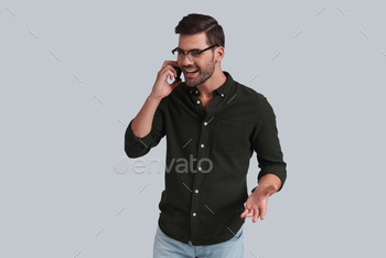 yeglasses talking on smart phone and smiling while standing against grey background