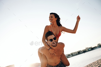 tractive girlfriend a piggy back ride while spending carefree time on the beach