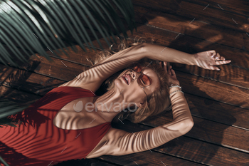 n in swimwear keeping eyes closed and mouth open while lying under the palm tree