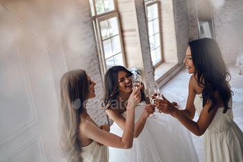 clicking glasses with her beautiful bridesmaids while standing in the fitting room