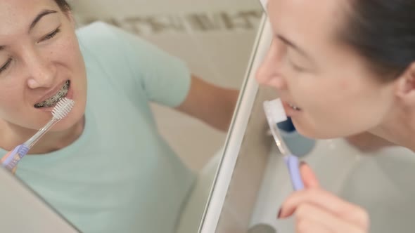 Young Woman Cleans Braces with a Brush Before Mirror Top View