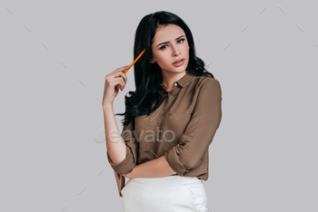 sual wear touching head with pencil and looking away while standing against grey background