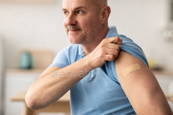 , antivirus campaign and health care. Smiling adult man showing shoulder with band aid after injection sitting at kitchen interior, free space