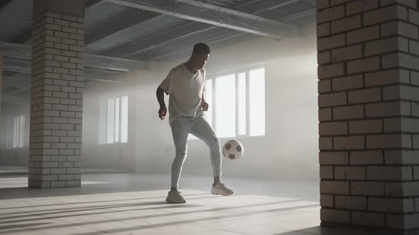 A Black Guy Trains with a Soccer Ball in an Underground Parking Lot in the Sunlight in Slow Motion