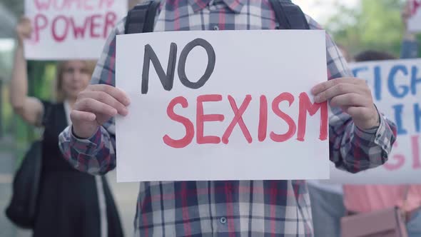 Unrecognizable Man Holding No Sexism Placard As Group of People Protesting at the Background. Anti