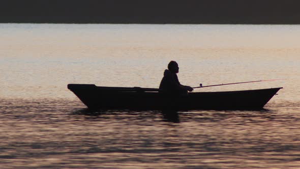 Man Sitting in a Boat and Fishing on Sunset