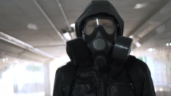 Man in Gas Mask Black Jacket with Hood Walking Through Long Tunnel Underpass