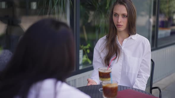 Young Emotional Caucasian Woman Sharing Talking with Friend Sitting at Table on Summer Terrace in