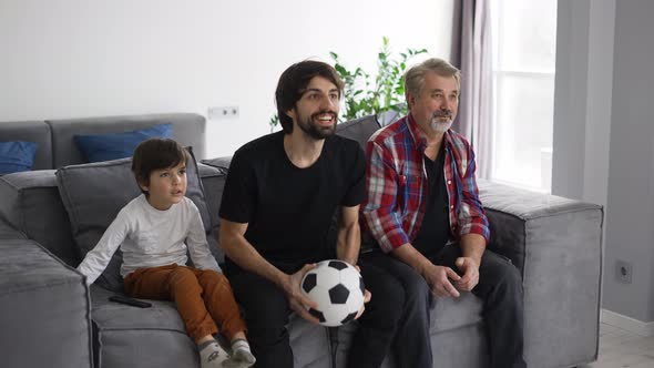 Three Generations of Men on Couch in Living Room Watch Football Match