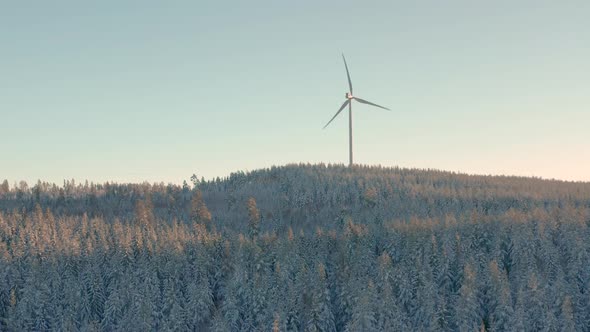 AERIAL - Wind turbine at sunrise in a snowy forest in Sweden, wide shot forward