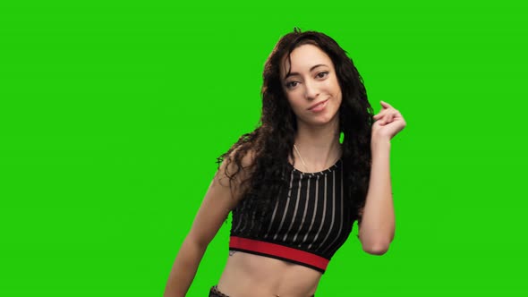 Cheerful long curly haired girl dancing on green screen background