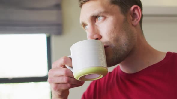 Thoughtful caucasian man is looking out the window and drinking coffee