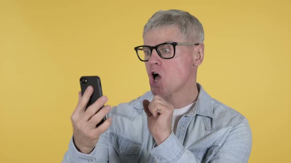 Shocked Casual Senior Man Using Smartphone, Yellow Background