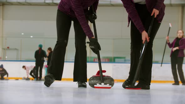 Curling Training Indoors - Leading Granite Stone on the Ice - Two Women Rubbing the Ice Before the