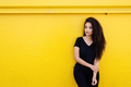 Stylish young black woman with long hair in black outfit in front of a vibrant yellow background - PhotoDune Item for Sale