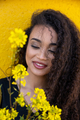 Beautiful woman with long curly hair standing behind yellow blooming flowers - PhotoDune Item for Sale