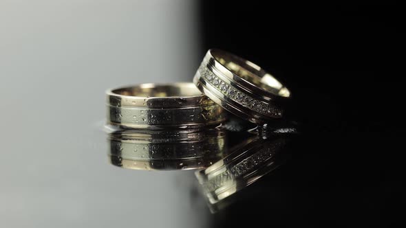 Wedding Rings on Black and White Water Surface Shining with Light. Close Up