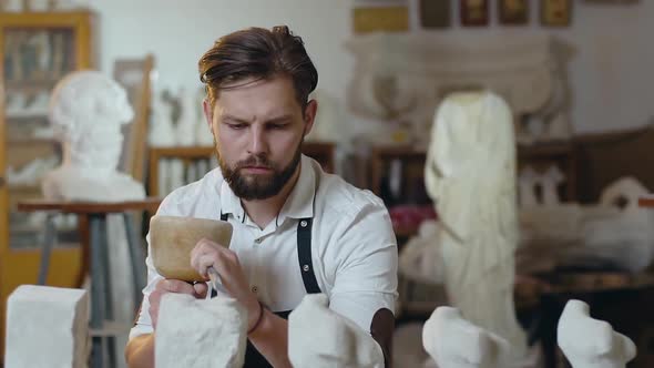 Bearded Stonemason Working in Studio with Mallet, Chisel and Limestone's Billets