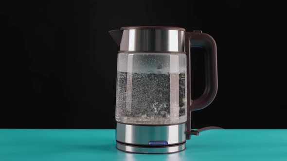A Modern Glass Electric Kettle on a Blue Table Black Background Filled with Water to Boil