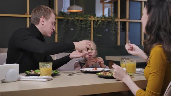 Happy Cute Girl Eating Pizza with Parents in Restaurant Indoors