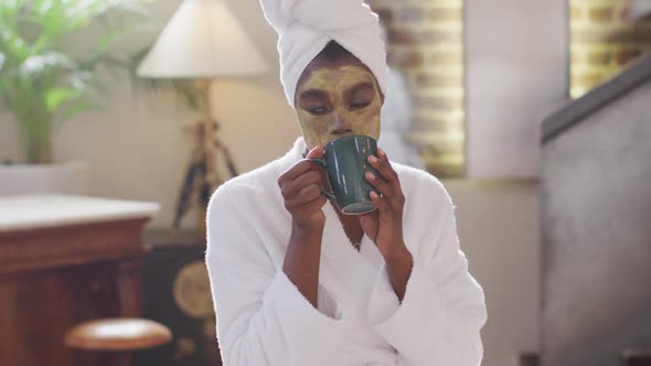 Eafrican american attractive woman with applied face mask drinking coffee and using laptop at home