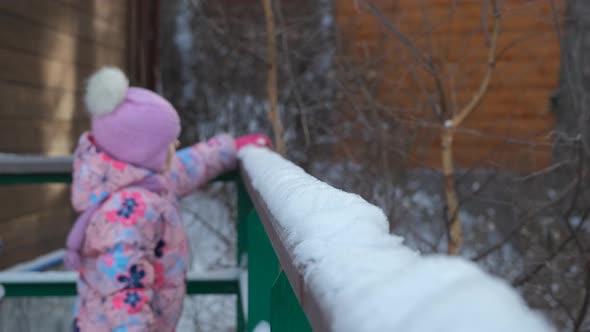 Little Girl Throwing Off Snow From Railing