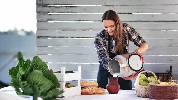 Smiling Farmer Female Pouring Homemade Milk From Metal Flask to Ceramic Mug