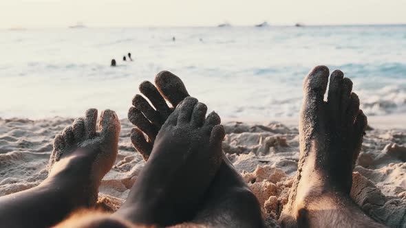 POV Feet of a Couple of Men and Women Lying on a Sandy Beach at Sunset By Ocean