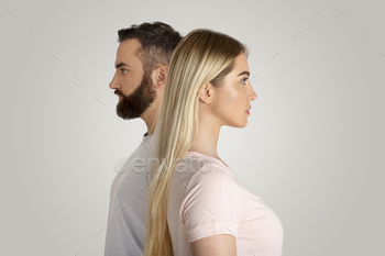 financial, social superiority, gender gap concept. Serious young guy and lady stand side by side and look in different directions, on gray background