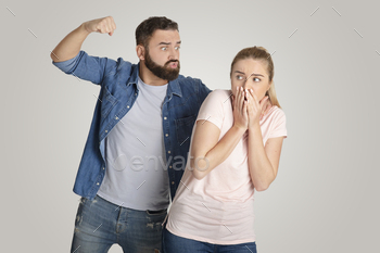 y. Aggressive angry young husband going to punch fist at frightened woman, she covers mouth with hands, isolated on gray background, free space