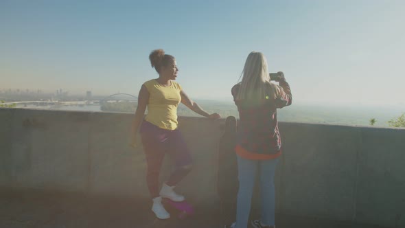 Active Female Skaters Recording Panoramic Cityscape on Phone at Dawn