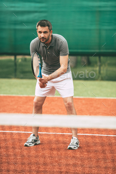 lothes carrying tennis racket and looking concentrated while standing on tennis court