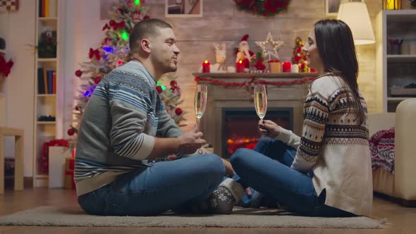 Couple Clinking a Glass of Champagne Sitting on the Carpet