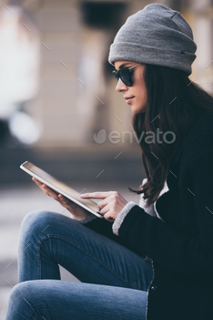  woman in sunglasses using her digital tablet while sitting outdoors