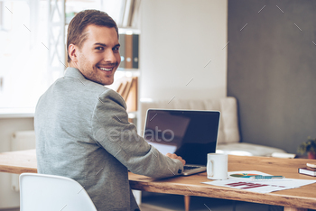 some man looking over shoulder at camera with smile while sitting at his working place