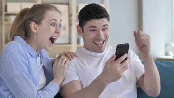 Young Couple Excited for Success While Using Smartphone