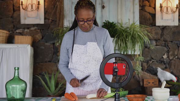African senior woman preparing food recipe while streaming online with mobile smartphone