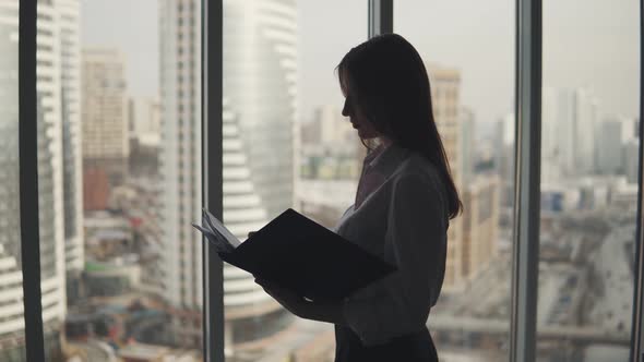 Silhouette of a Business Woman on the Background of Skyscrapers. a Girl Is Standing By the Window