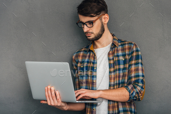 laptop and looking concentrated while standing against grey background