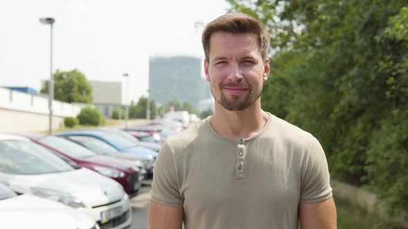 A Young Handsome Man Smiles at the Camera in a Parking Lot in an Urban Area