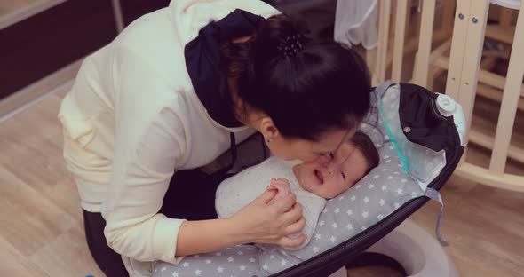 Happy Mom Holds the Newborn Baby By the Handles and Kisses