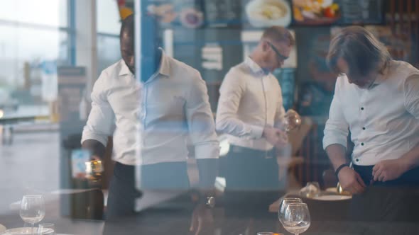 View Through Window of Diverse Waiters in Uniform Serving Tables in Restaurant