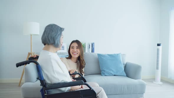 Asian young daughter support  help and take care old disabled woman on wheelchair at home.